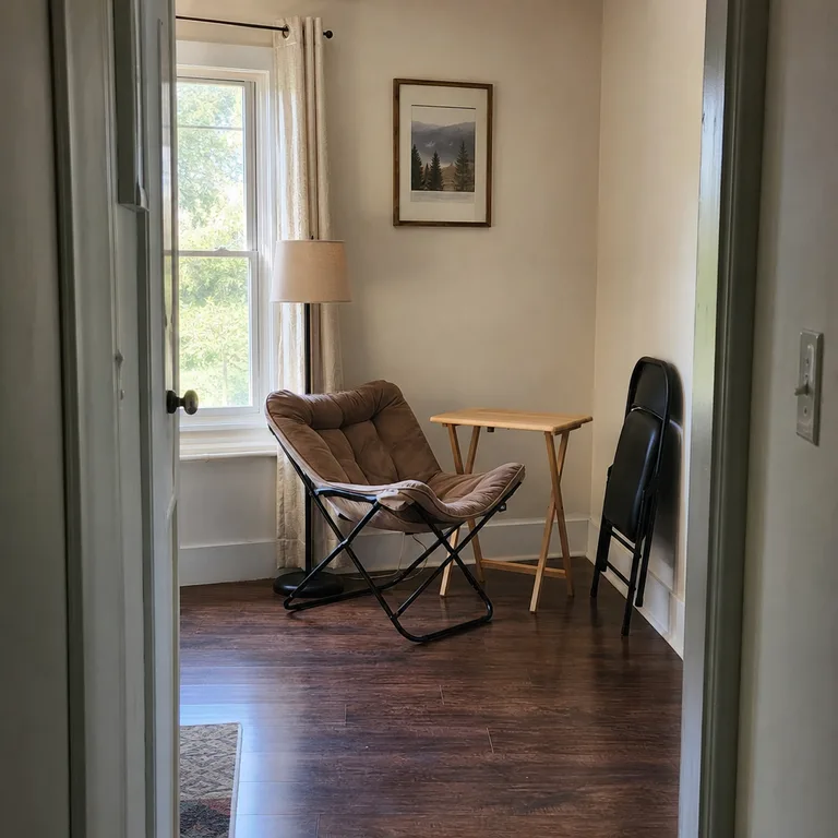 Cushioned folding chair, portable lamp, and tray table in a flexible living-room reading corner.