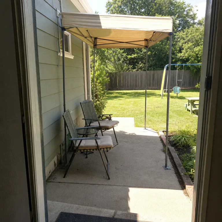 A small folding canopy shades two patio chairs while the nearby lawn remains open for play.