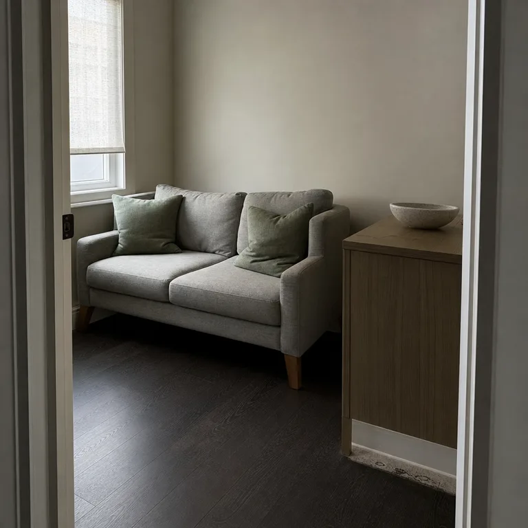 Soft sage pillows and pale stoneware accessories above nearly black flooring in a rental living room.