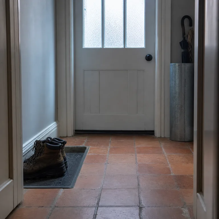 Wet boots sit in a lined recessed floor niche beside a front door.