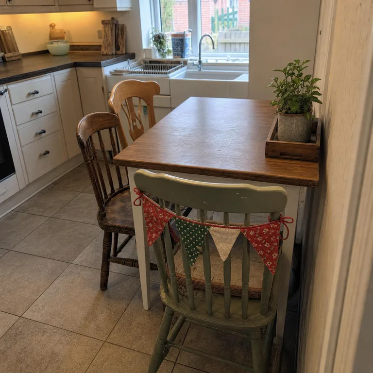 Short red, green, and cream fabric bunting tied across the upper back of a painted wooden dining chair.