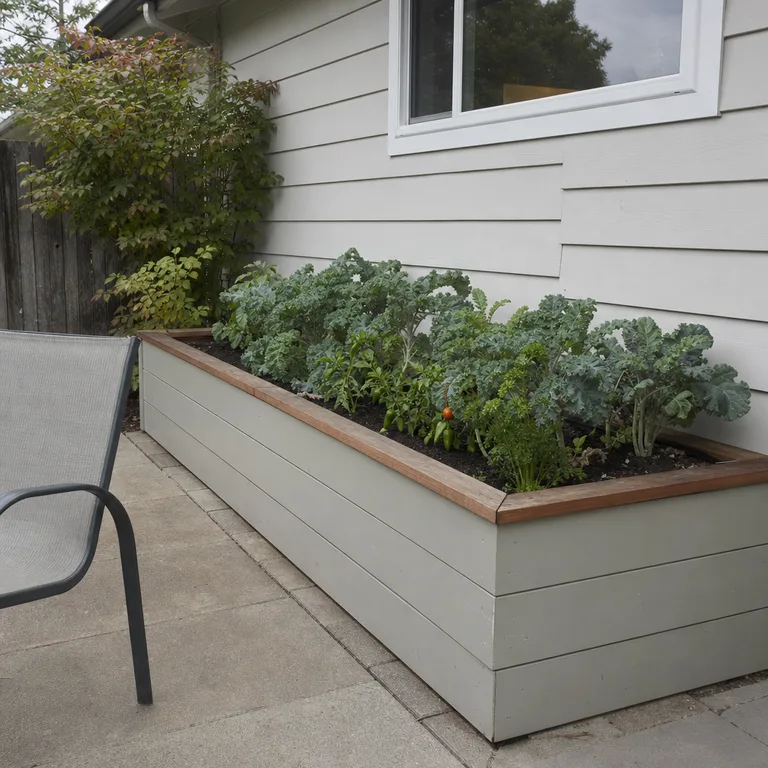 A waist-high raised bed with kale and pepper plants beside a small patio.