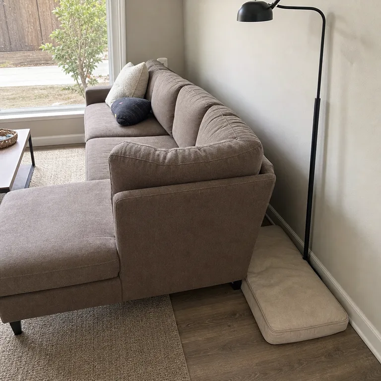 Rectangular pet cushion in the protected gap behind the chaise section of a small sectional sofa.