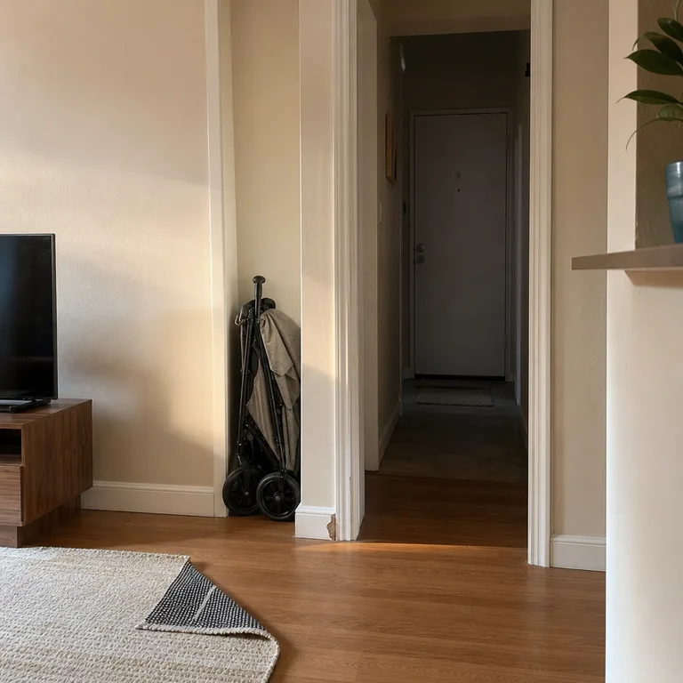 Folded stroller parked in a living-room niche beside the doorway, leaving the entry hall open.