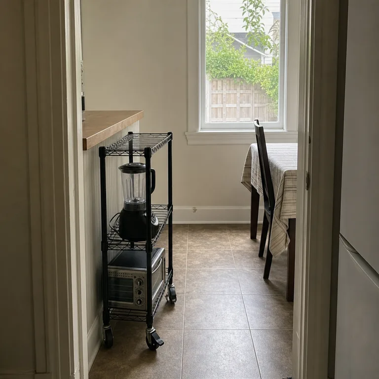 A compact utility cart holds a toaster oven and blender beside a small kitchen counter.