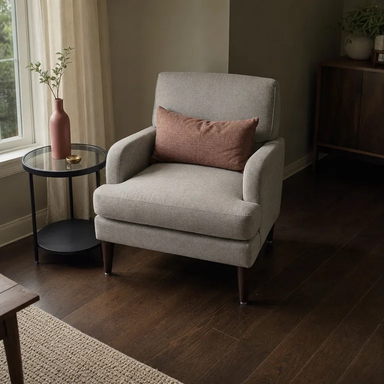 Pale gray chair with a dusty rose pillow on espresso brown flooring in a compact living room.