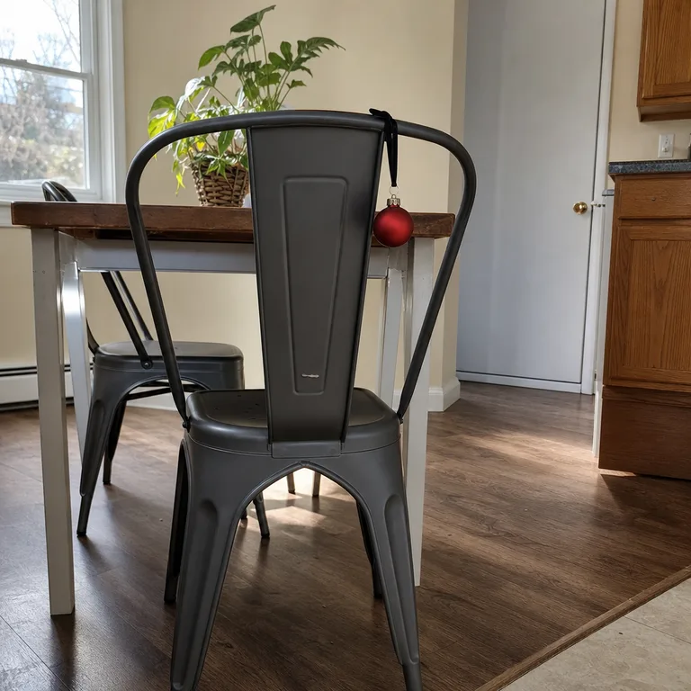 A single matte red shatter-resistant ornament tied below the top rail of a metal dining chair.