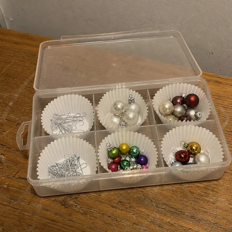 Ornament hooks and spare small holiday hardware sorted in a reused takeout container.