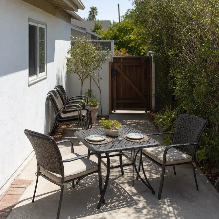 A small patio table for two with extra stackable chairs stored against the wall.