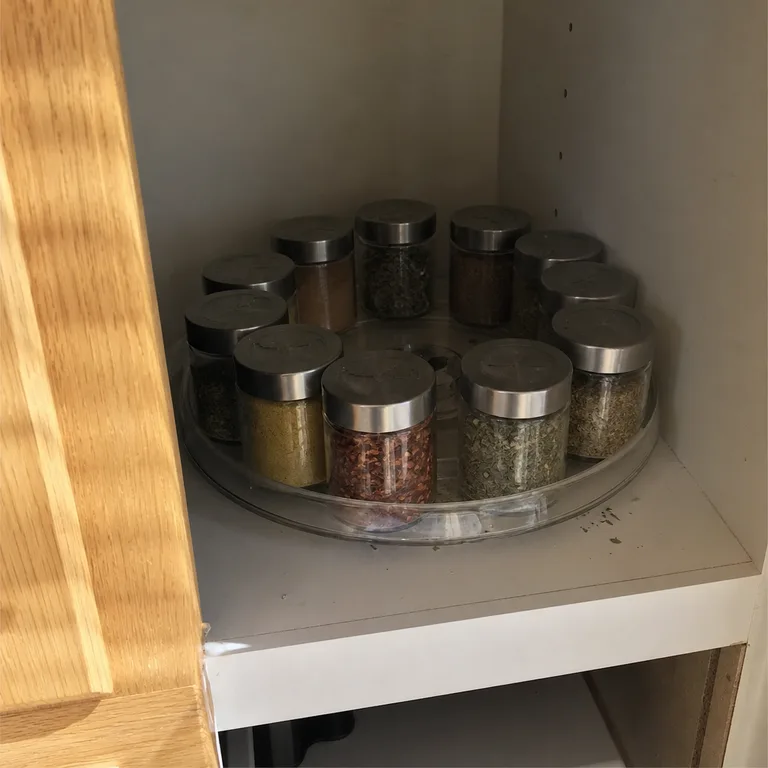 Mixed spice jars arranged on a small clear turntable in a deep cabinet.