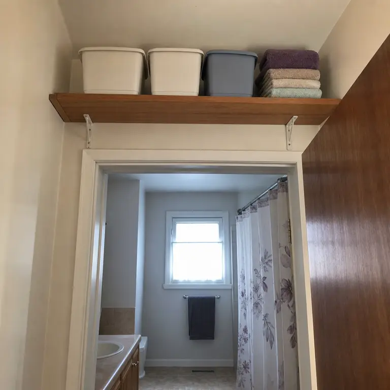 High shelf above a bathroom door holding bins of backup supplies and towels.