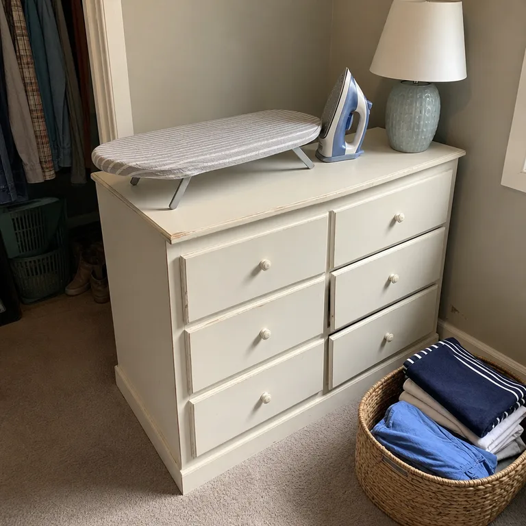 A compact ironing board opened on a cleared sturdy dresser in a small bedroom.