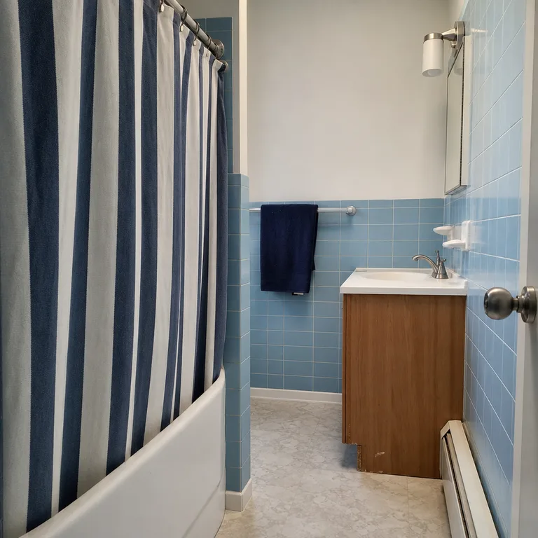 Navy striped shower curtain bringing contrast to blue tile in a narrow bathroom.