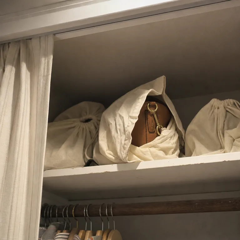 Handbags in breathable dust covers on an upper bedroom closet shelf.