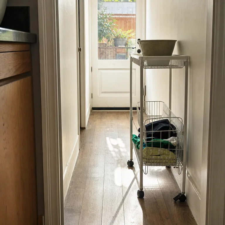 A slim rolling cart stores folded reusable bags in its lower basket near a kitchen door.