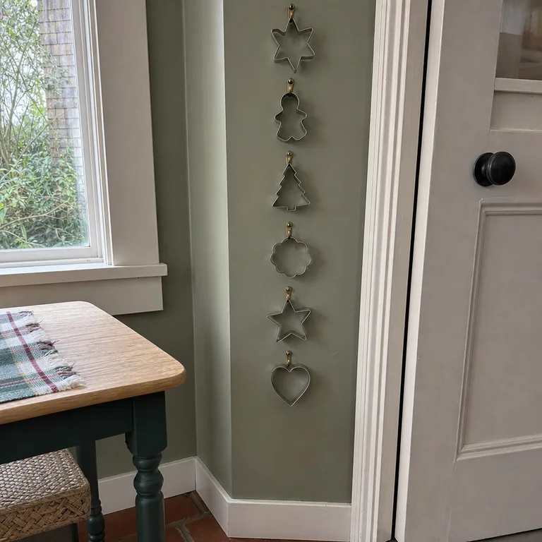 Christmas-shaped metal cookie cutters are displayed vertically on a narrow kitchen wall.