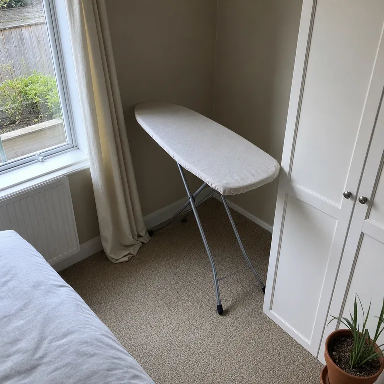 A narrow ironing board set up in an unused bedroom corner away from the bed.