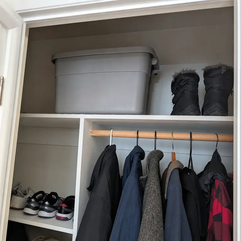 Lidded tote storing seasonal shoes on the top shelf of an entry closet.