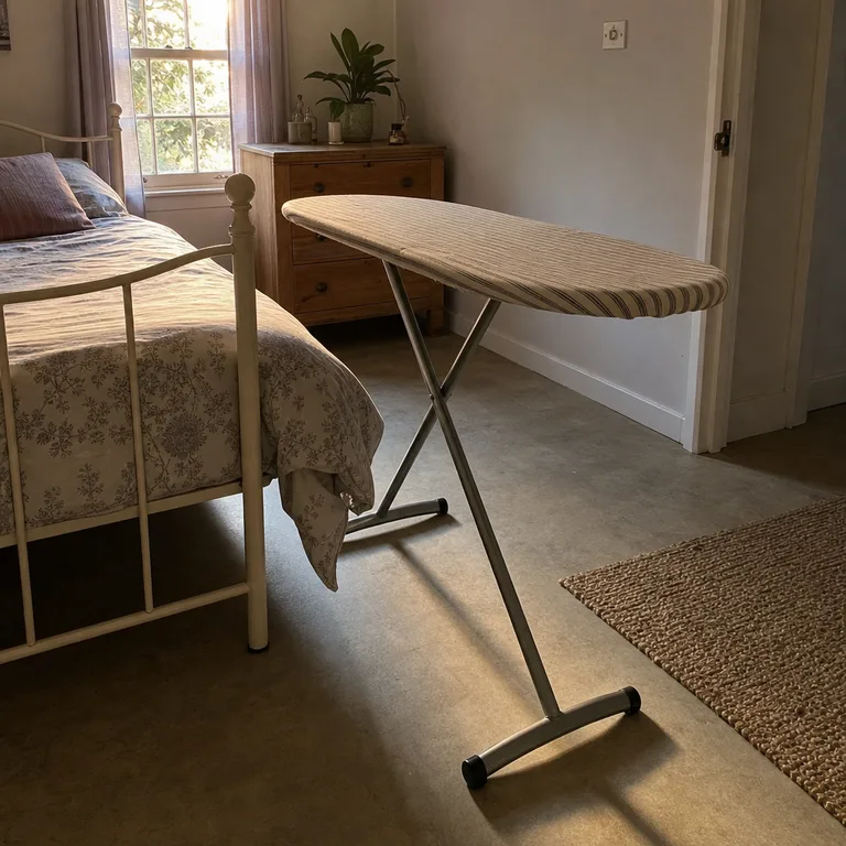 A full folding ironing board positioned in the open space at the foot of a bed.