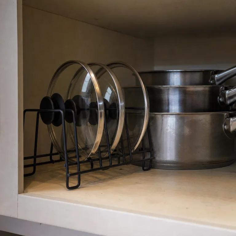 Small pot lids stored upright in a metal file sorter on a pantry shelf.