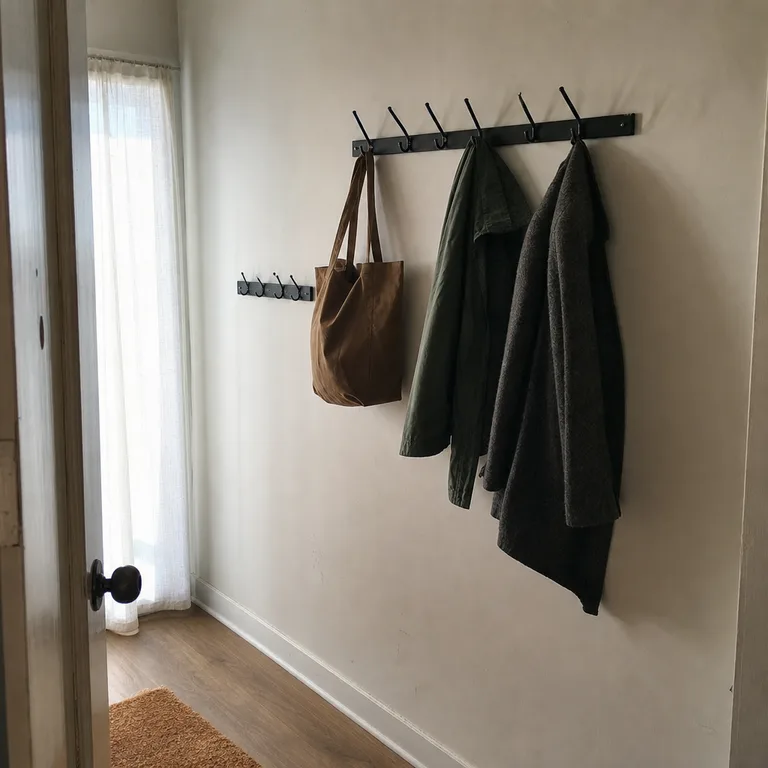 Narrow apartment entry with two staggered wall hook rails holding coats and bags beside the door.