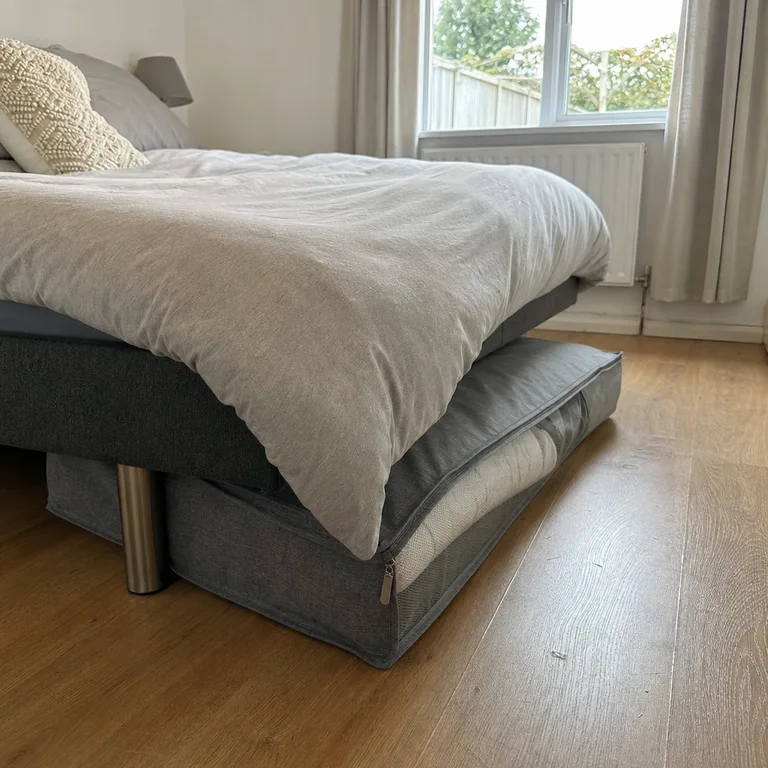 A fabric zip bag holding a bulky duvet under a bed with limited clearance.