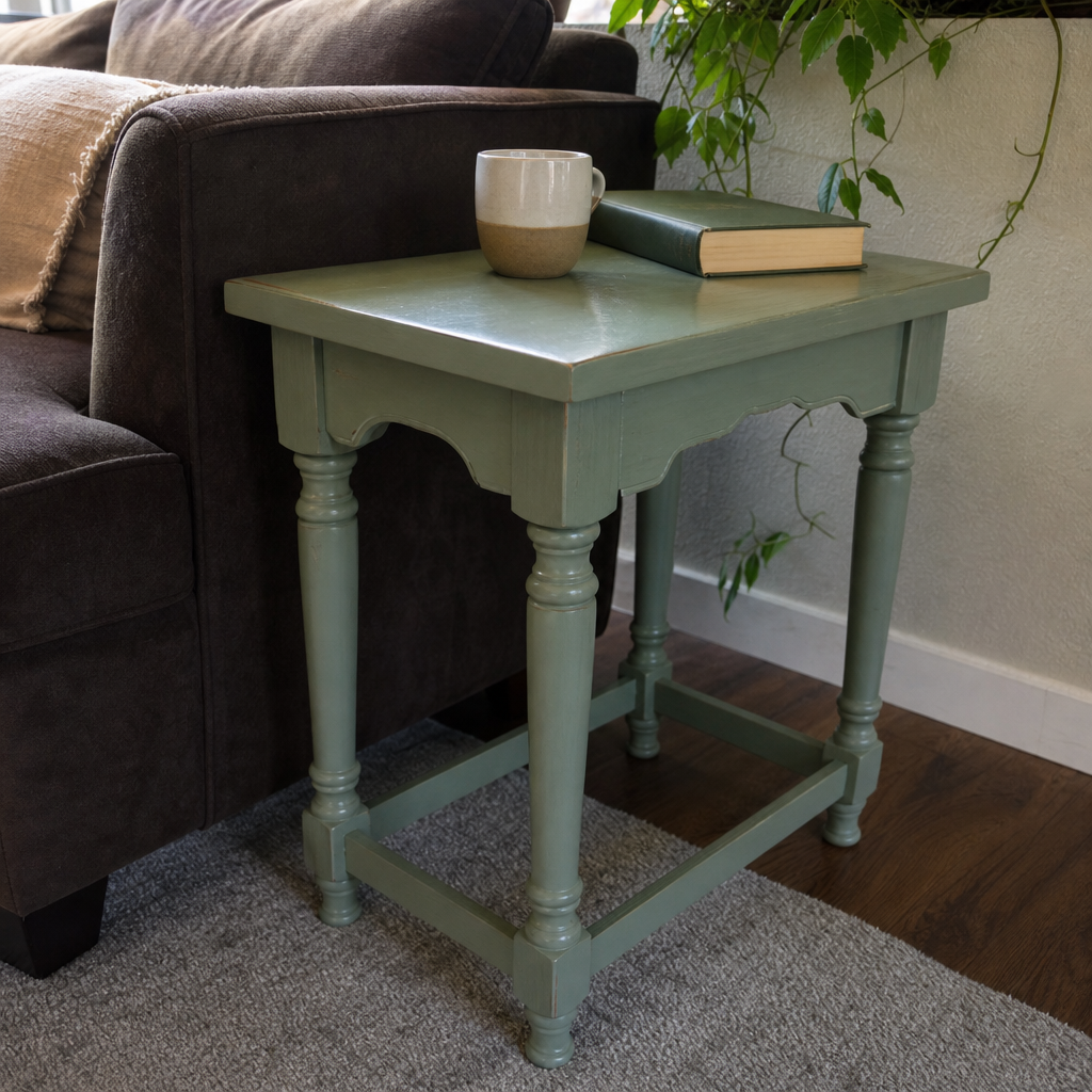 Sage green painted side table beside a dark brown sofa.